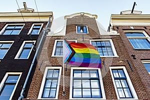 Old Dutch canal houses in Amsterdam with a Progress Pride Flag on their facades during Gay Pride Amsterdam