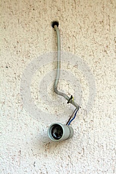 Old E27 type ceramic light bulb socket hanging from brown and blue electrical wires insulated in grey cable connected to family