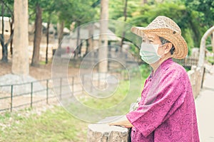 Old elder woman wearing woman wearing medical mask resting in garden. asian elderly senior relaxing outdoors