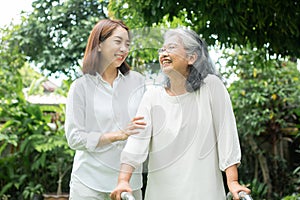 An old elderly Asian woman uses a walker and walking in the backyard with her daughter.  Concept of happy retirement With care
