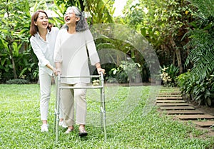 An old elderly Asian woman uses a walker and walking in the backyard with her daughter.  Concept of happy retirement With care