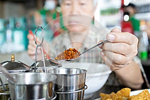 Old elderly eat food that tastes hot spicy,add flavor to food with chili powder from condiment,asian senior woman using a spoon to photo