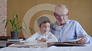 Old elderly man in glasses for vision together with his grandson enjoy happy memories watching a family photo album