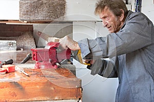 Old elderly man sawing in workshop shed