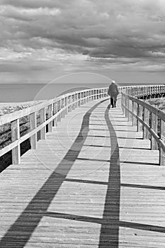 Old elderly man walking on a boardwalk along the ocean. A feeling of solitude. photo