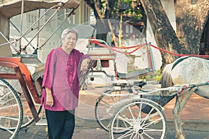 Old elderly senior elder woman with horse rickshaw serving tourist. old vintage retro asian tricycle