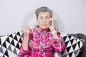 An old elderly woman grandmother with gray hair sits at home on the couch using the hand phone, a telephone conversation