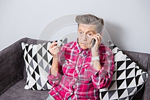 An old elderly woman grandmother with gray hair sits at home on the couch using the hand phone, a telephone conversation