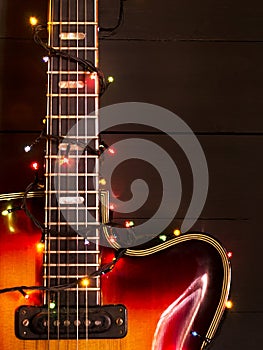 Old electric guitar with a lighted garland on a dark background. Greeting, Christmas, New Year greeting card. Copy space.