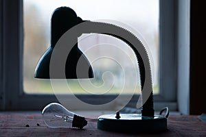 Old electric lamp with burned-out light bulb lying on the table in front of a window