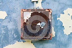 The old electric shield hangs on the exfoliating wall of the house, a rusty metal box hanging on the wall