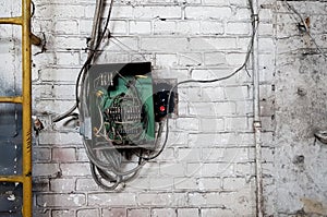 Old electrical panel on the wall of the house. Electric cables stick out from the electric panel on the white brick wall of the