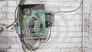 Old electrical panel on the wall of the house. Electric cables stick out from the electric panel on the white brick wall of the