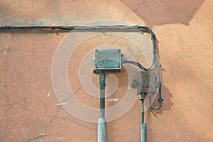 Old electrical power and telephone cables fixed to a plaster wall with metal protection junction box