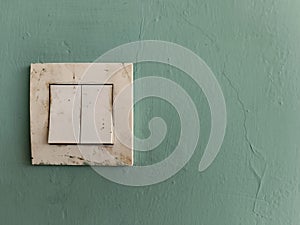 Old electrical socket and light switch on a green painted wall, showing signs of dirt and wear, suitable