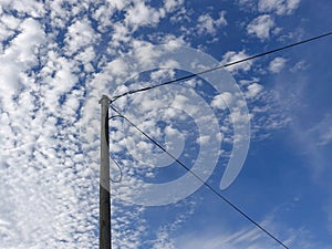 Old electricity wooden pylon and wires with blue cloudy sky