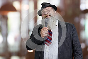 Old elegant man talking in microphone on abstract bokeh background.