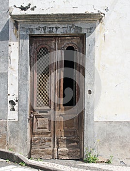 Old elegant weathered ornate wooden brown door with carved panels and missing grille in a white abandoned house