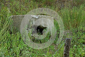 The old embrasure of the military pillbox in the grass behind the barbed wire