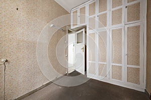 An old empty bedroom with a built in wardrobe that covers an entire wall from side to side and top to bottom with papered white