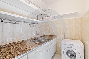 Old empty kitchen with shelves, tiled walls, marble countertop and washing machine.