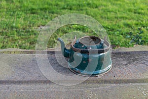 Old enameled kettle on the metal sheet on the background of green grass.