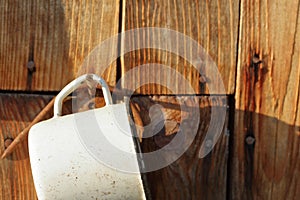 An old enameled mug hangs on a nail. A nail is driven into the wall of an old barn from planks