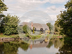 Old english historic cottage seen over a lake with reflections