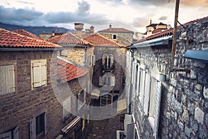 Vintage european city street with orange tile roofs and ancient building facade in front of dramatic sunset sky with antique arch