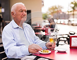 Old man on restaurant terrace with glass of beer