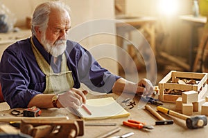 Old experienced carpenter sitting at the messy table at workplace