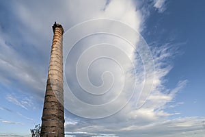 An old factory brick chimney against a cloudy blue sky