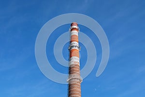 Old factory striped, orange, brown, chimney on a blue sky background