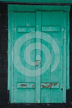 Old faded green shutters locked on a black cottage