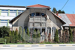 Old family house with dilapidated facade and wooden porch surrounded with cypress trees in front and office buildings in