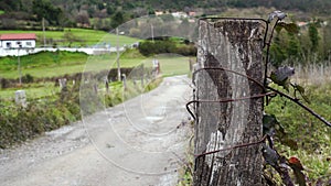 Old farm fence with a weathered wooden post and rusty barbed wire along a dirt road.