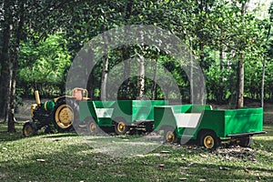 Old farm tractor with carts used for agricultural transport or passenger use in a green forest background at a farm on vintage