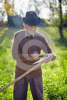 Old farmer sharpening scythe