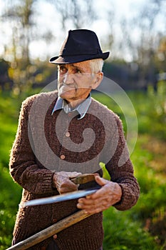 Old farmer sharpening scythe