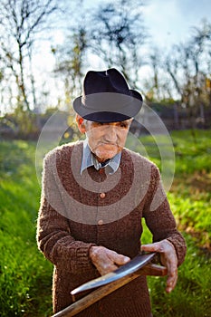 Old farmer sharpening scythe