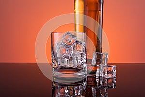 Old fashion glass and bottle with whisky drink on warm, orange background and wood