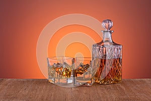 Old fashion glass and carafe with whisky drink on warm, orange background and wood