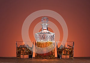 Old fashion glass and carafe with whisky drink on warm, orange background and wood