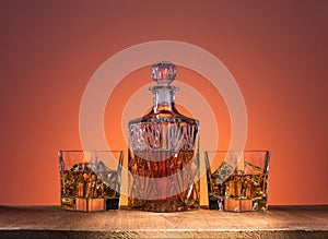 Old fashion glass and carafe with whisky drink on warm, orange background and wood