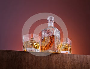 Old fashion glass and carafe with whisky drink on warm, orange background and wood