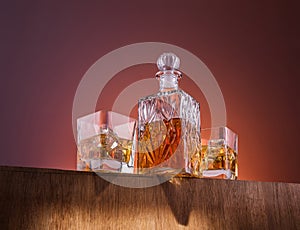 Old fashion glass and carafe with whisky drink on warm, orange background and wood