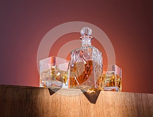 Old fashion glass and carafe with whisky drink on warm, orange background and wood