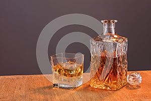 Old fashion glass and carafe with whisky drink on warm, orange background and wood