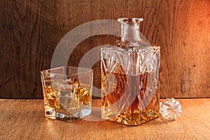 Old fashion glass and carafe with whisky drink on warm, orange background and wood