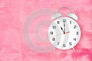 Old fashioned alarm clock with twin bells and ringer showing 11 eleven o'clock on pink background photo